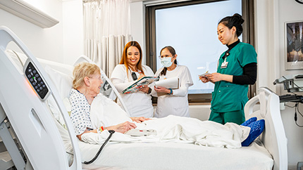 Nurses and intern speaking with a patient in a hospital room.